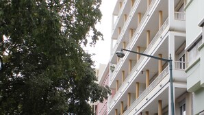 A multi-story building with balconies, a street with parked cars, and a tree on the left. - Residencial Lord (Lisbon)