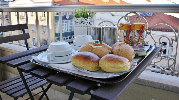 A balcony with a table set for breakfast, including bread rolls, a teapot, cups, and a plant. - Residencial Lord (Lisbon)