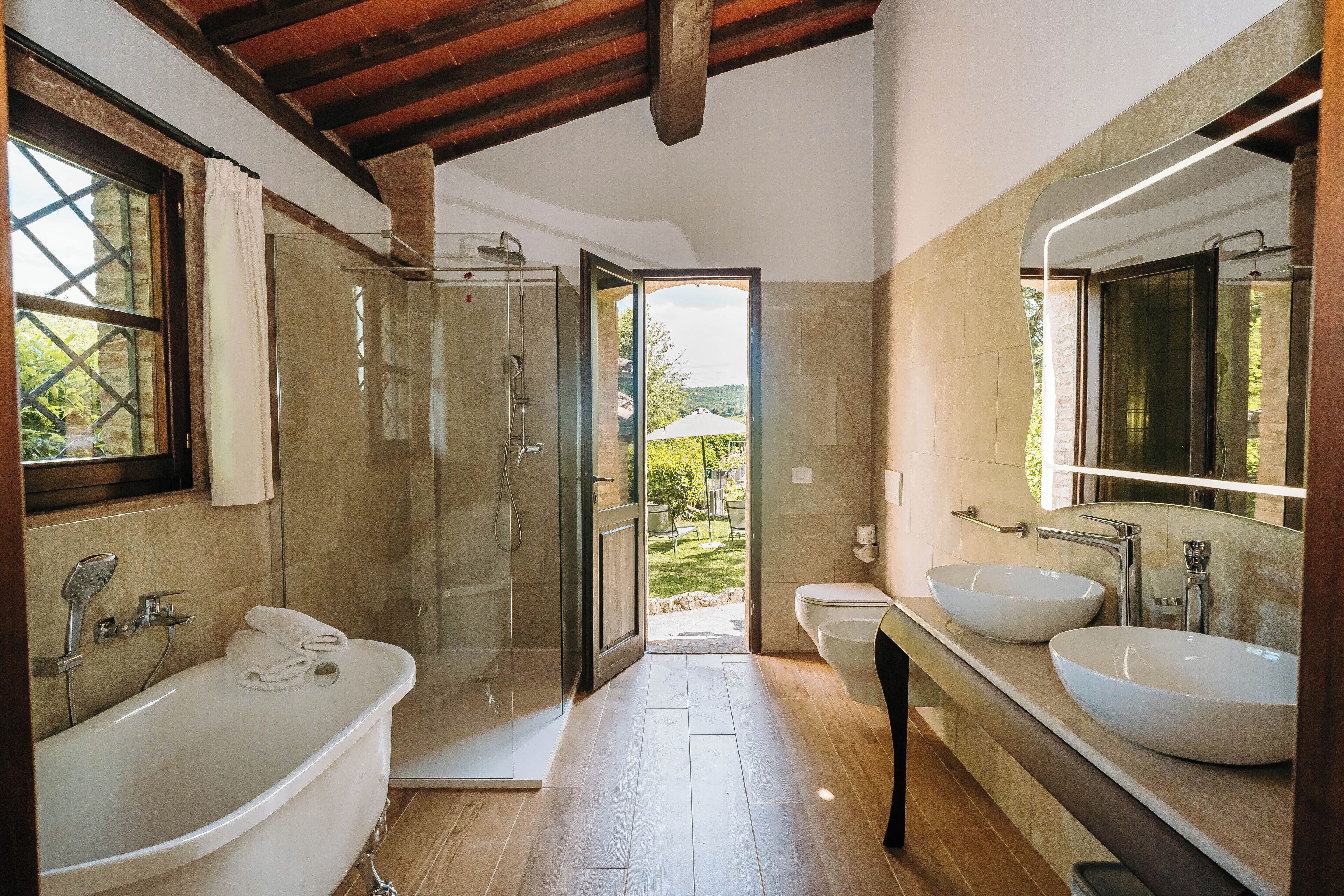 A modern bathroom with a large bathtub, two sinks, and a glass-enclosed shower.