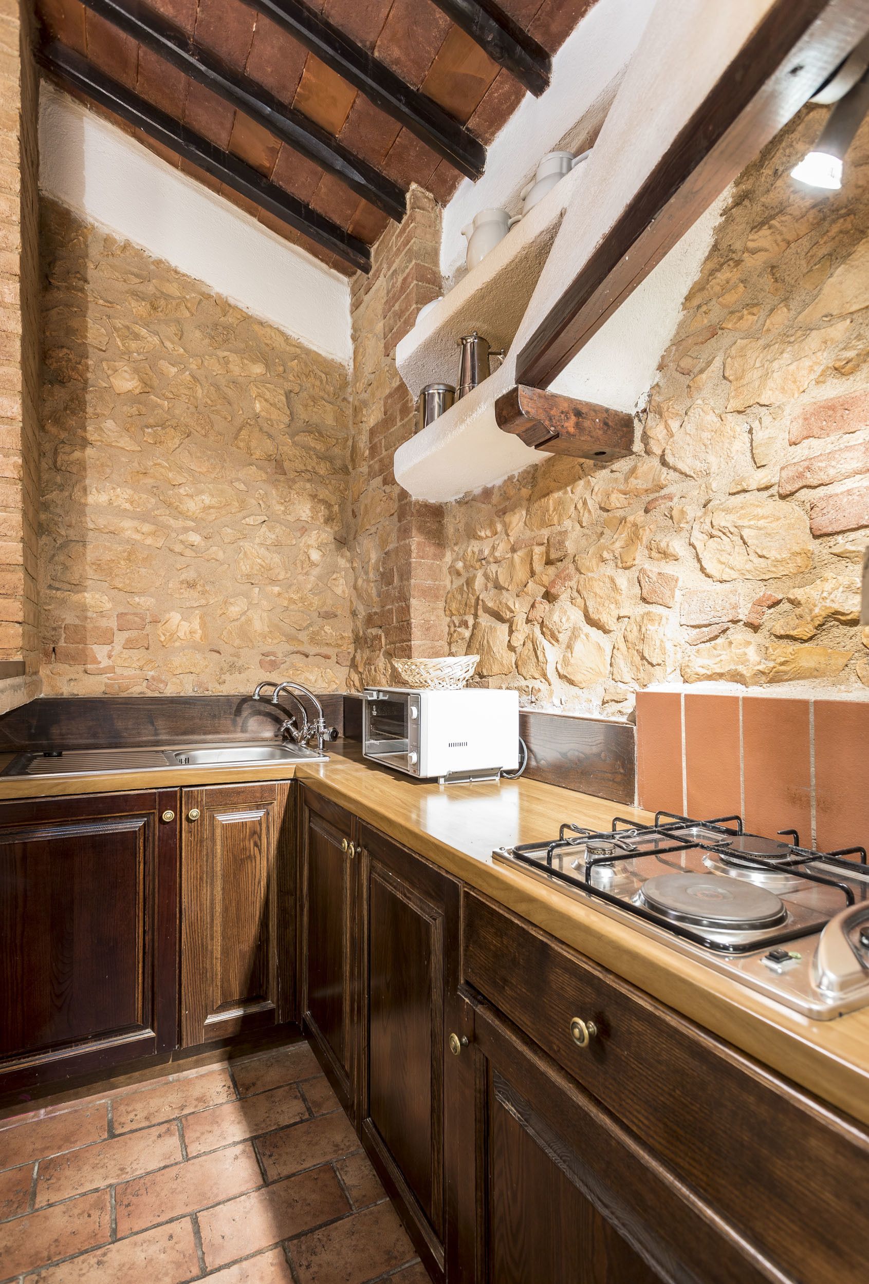 A kitchen with stone walls, wooden cabinets, a gas stove, and a microwave.