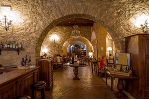 Ein rustikaler Innenraum mit Steinwänden, Holzmöbeln und einem zentralen Tisch.