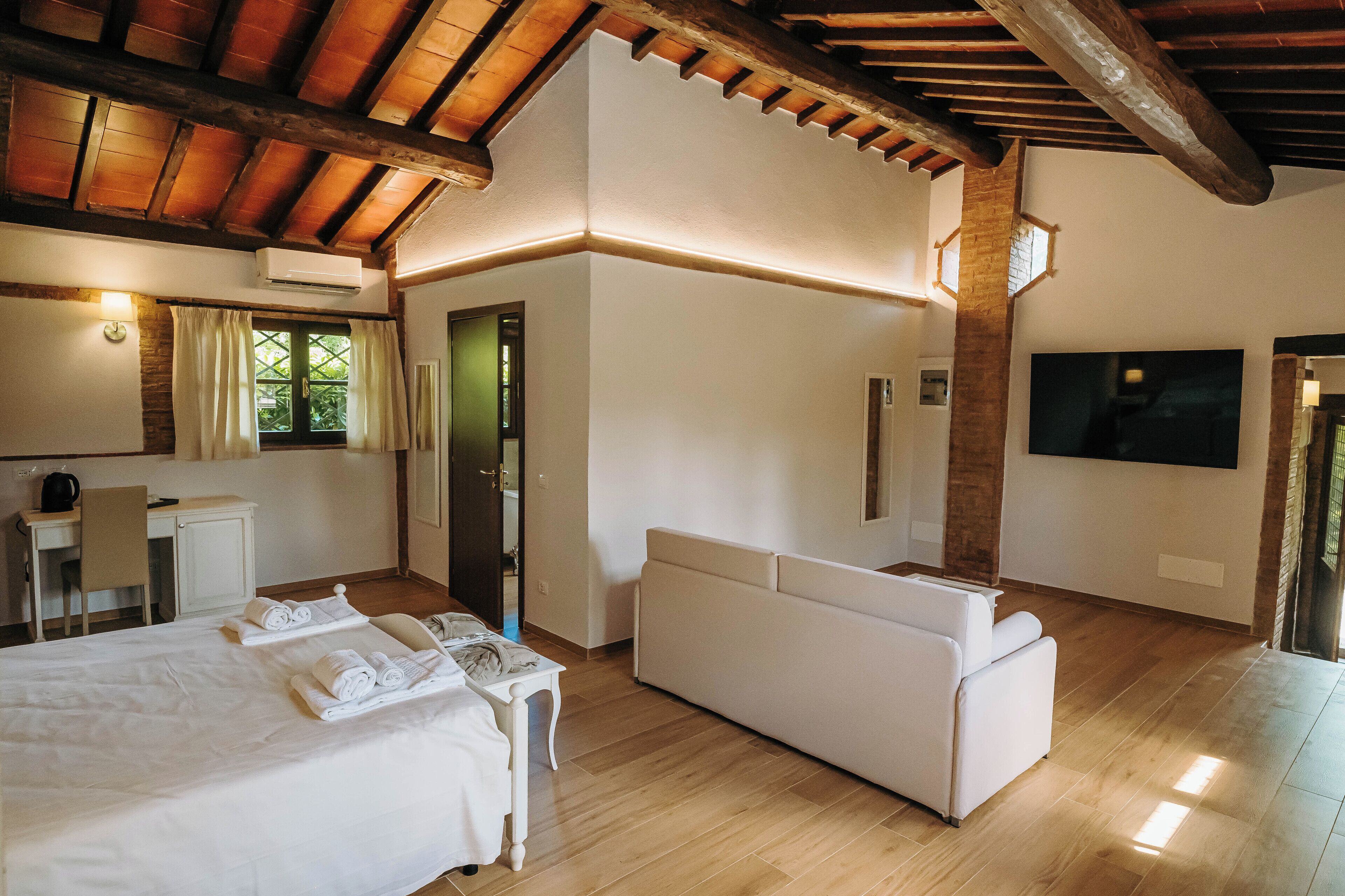 Een ruime slaapkamer met een groot bed, een slaapbank, een bureau en een aan de muur bevestigde televisie.