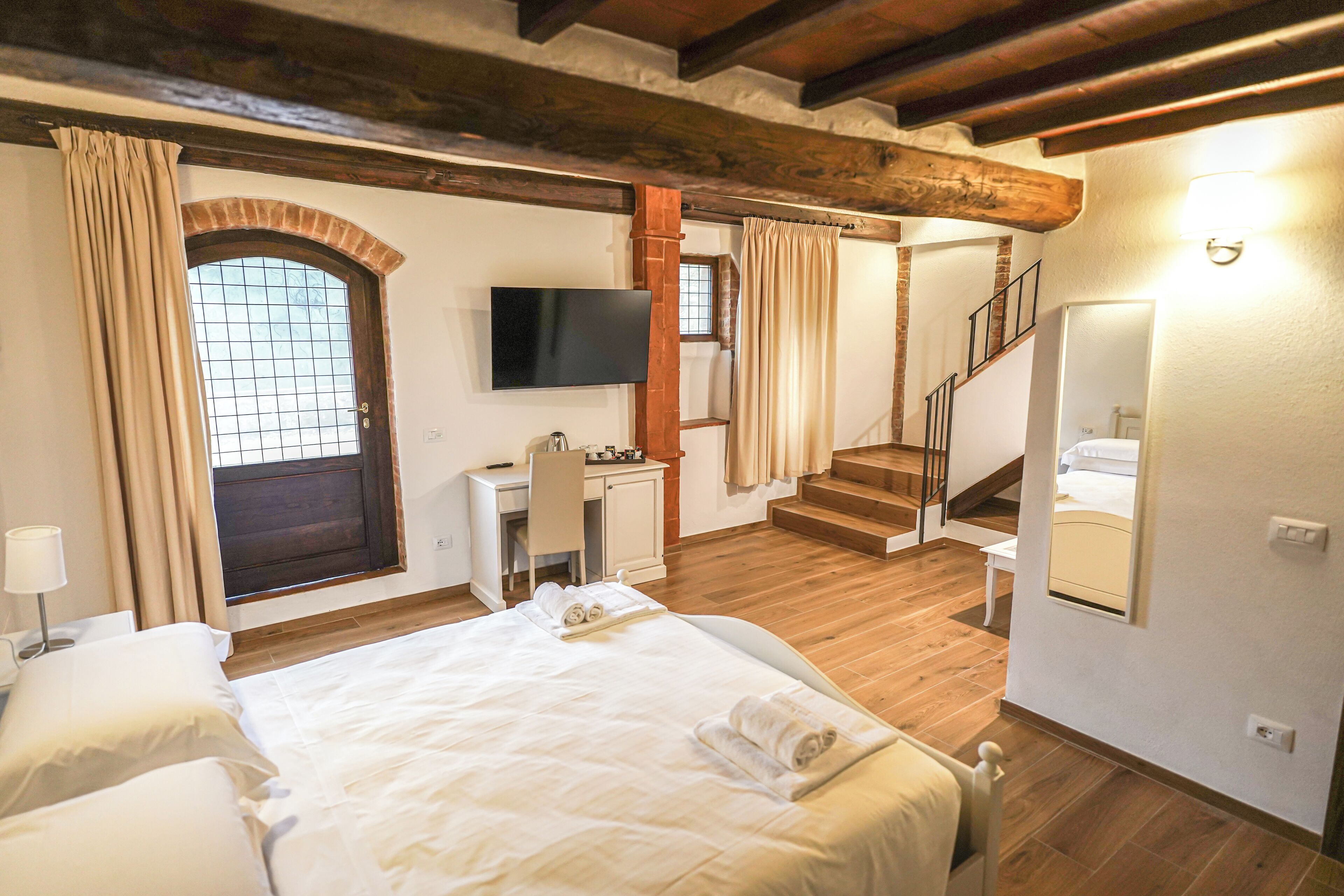 A bedroom with a large bed, a desk, a TV, and a staircase leading to another room.