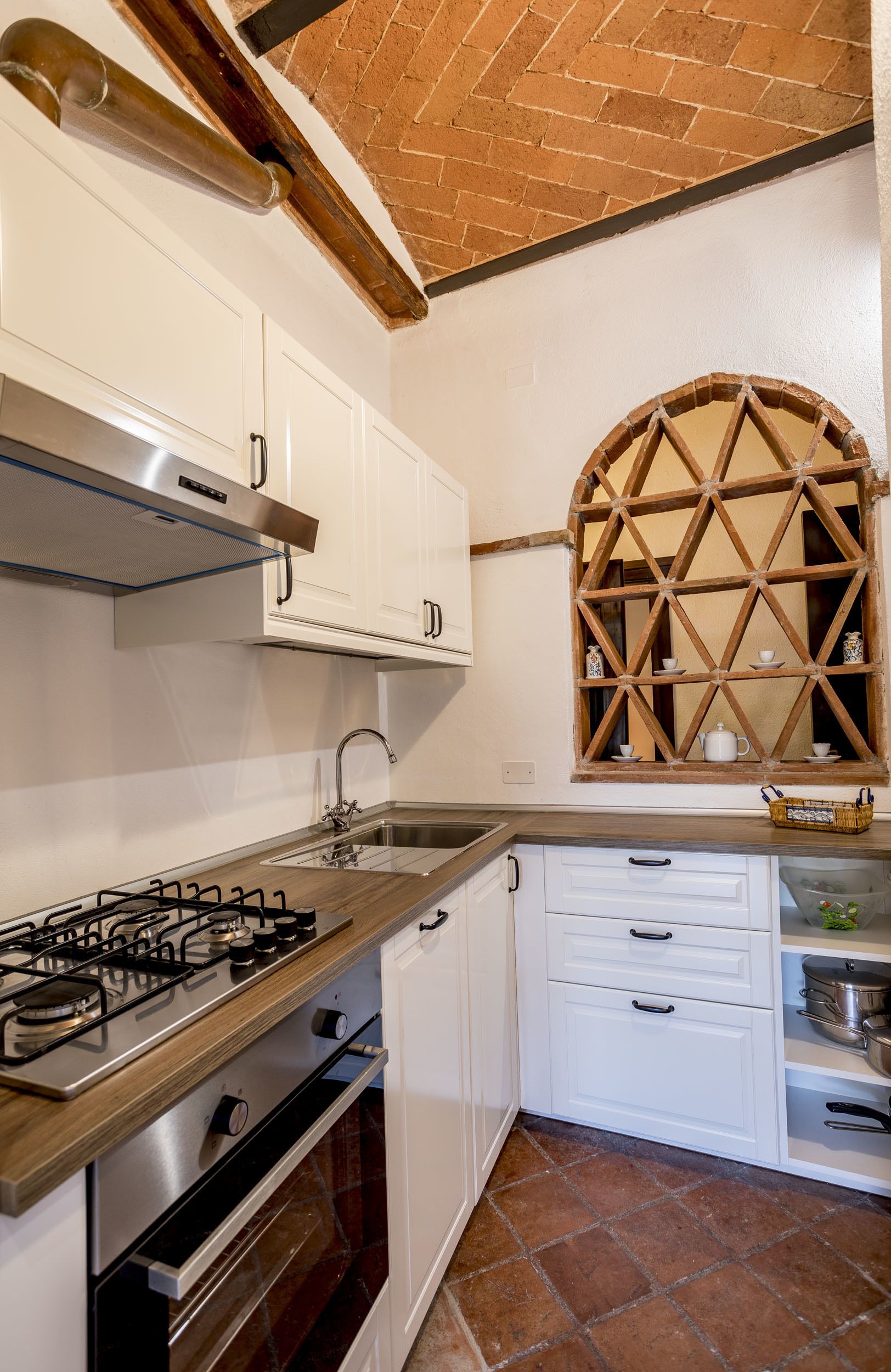 A kitchen with white cabinets, a gas stove, a stainless steel sink, and a wooden window with a lattice design.