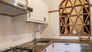 A kitchen with white cabinets, a gas stove, a stainless steel sink, and a wooden window with a lattice design.