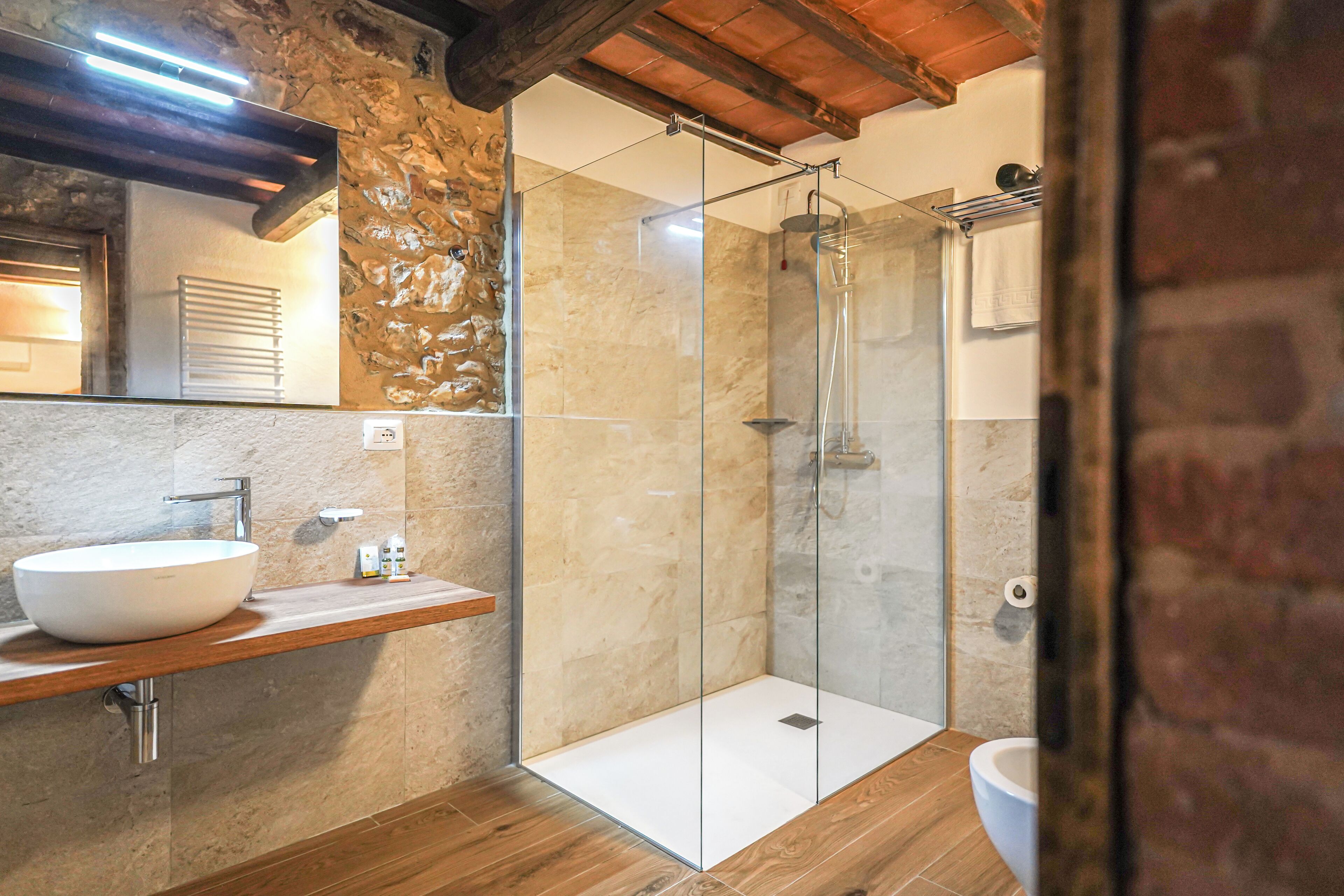 Een moderne badkamer met een stenen muur, een houten wastafelmeubel, een douche met glazen wanden en een wit toilet.