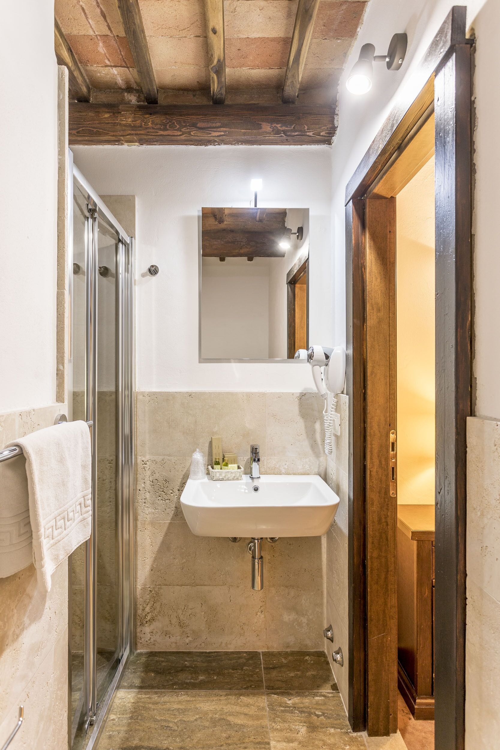 Une salle de bain avec une douche à parois de verre, un lavabo avec un miroir au-dessus et une porte en bois donnant sur une autre pièce.