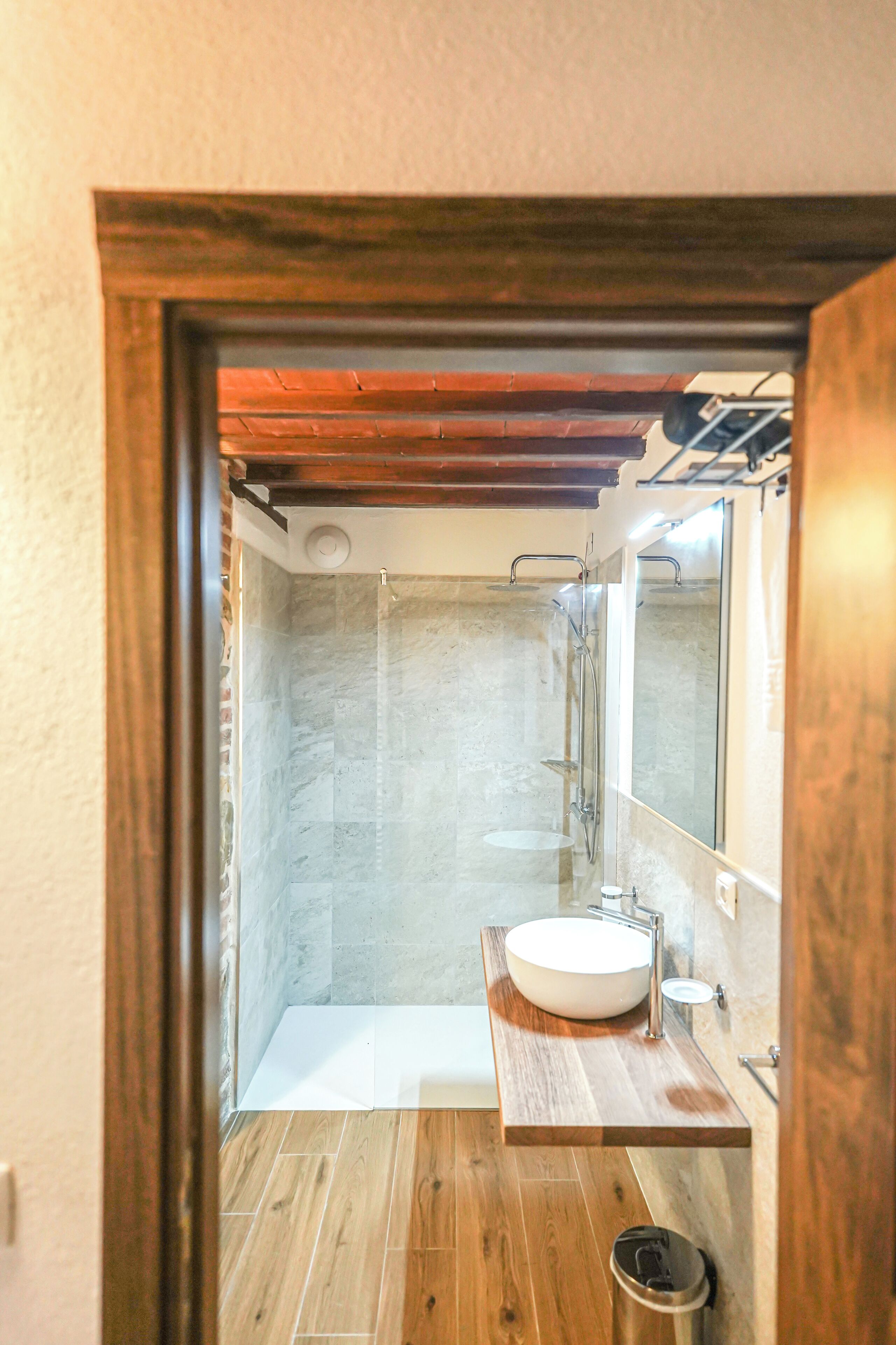 A modern bathroom with a wooden vanity, a white sink, and a glass shower enclosure.