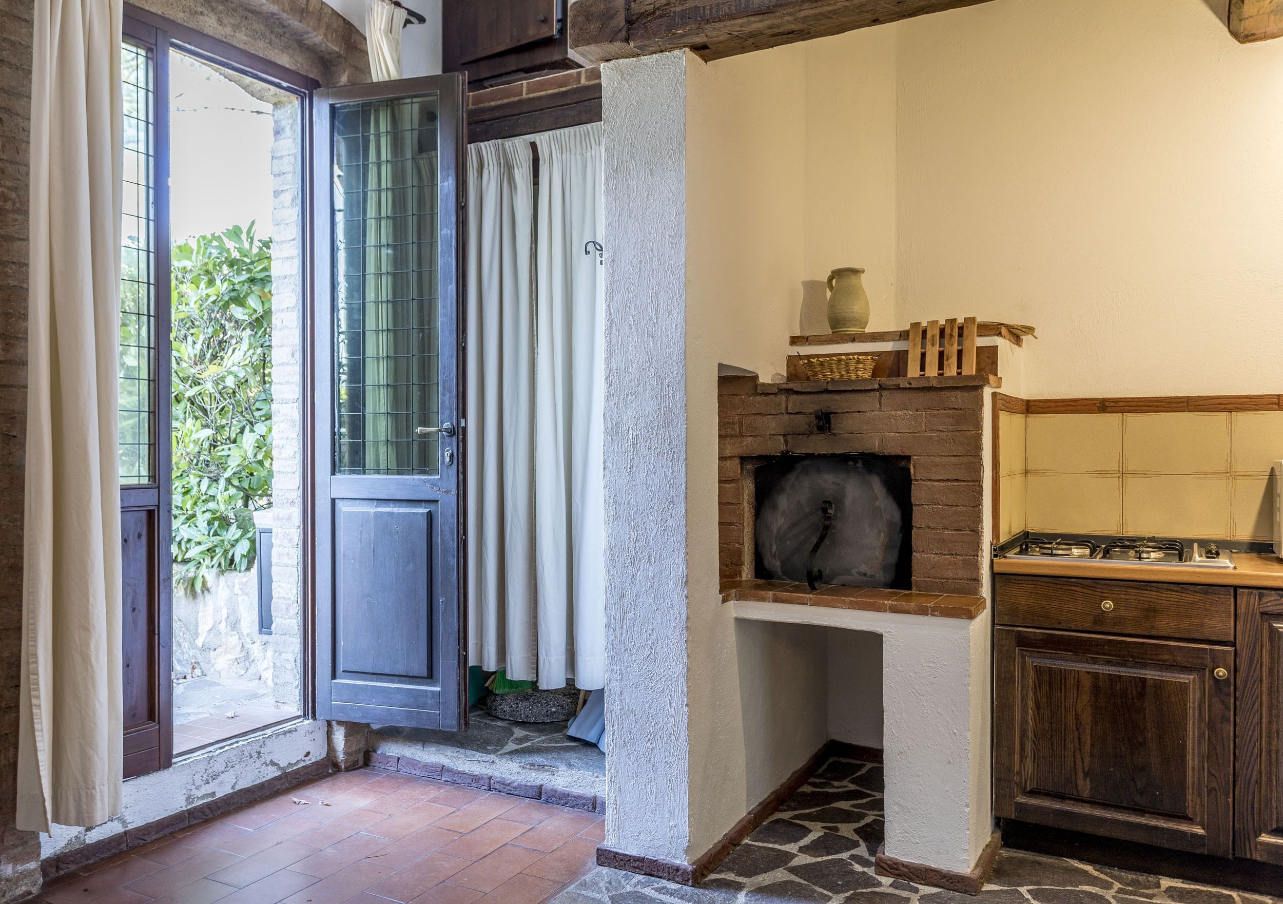 A rustic kitchen with a stone floor, wooden cabinets, and a brick fireplace.