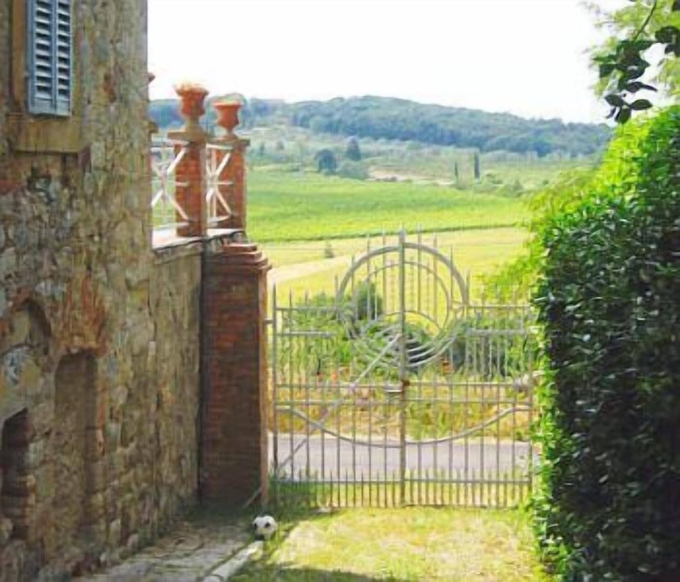 A rustic stone building with a metal gate leading to a green field.