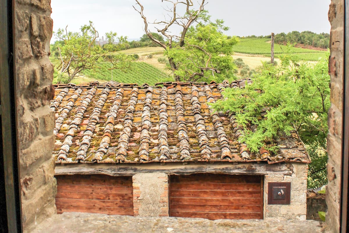 Un bâtiment rustique, doté d’un toit en tuiles et de portes en bois, vu à travers une fenêtre en arc de cercle.