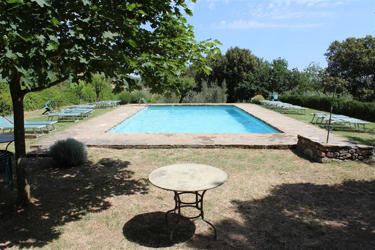 Ein rechteckiger Swimmingpool mit Steinbordierung, umgeben von Liegestühlen und einem kleinen Tisch in einer sonnigen Außenanlage.