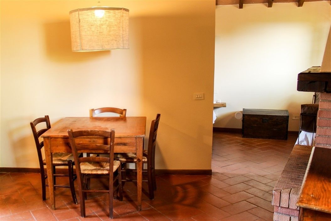 A dining area with a wooden table and chairs, a hanging lamp, and a brick fireplace.
