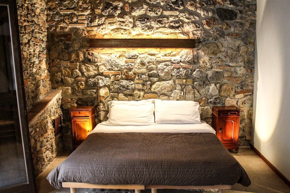 Une chambre avec un mur en pierre, un cadre de lit en bois et deux tables de chevet en bois.