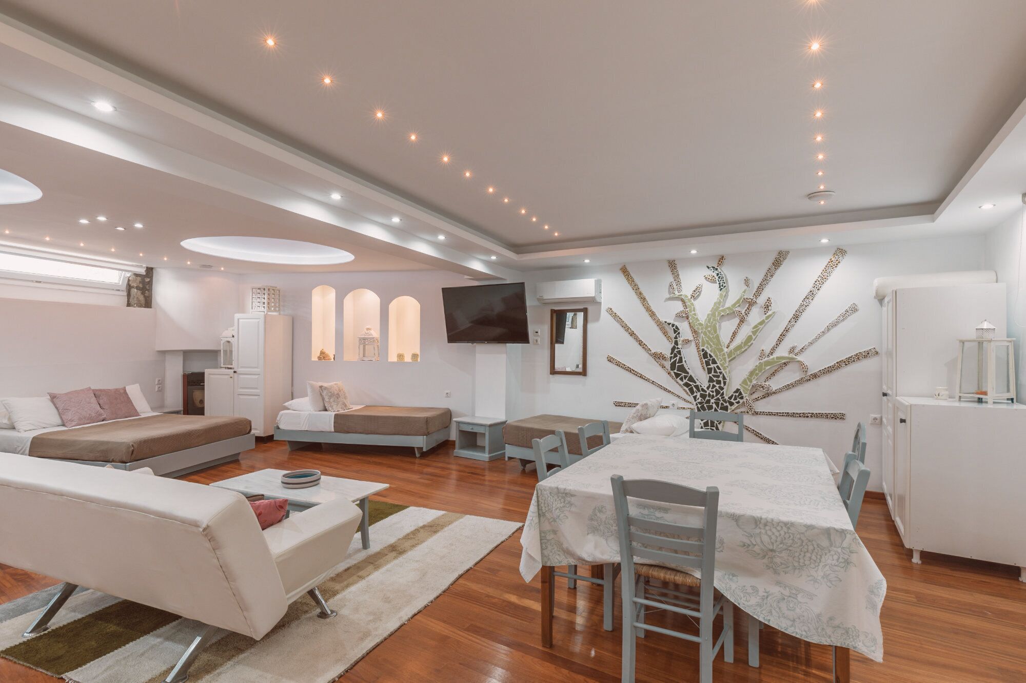 A modern, well-lit living room with a sofa, a dining table with chairs, and a decorative wall piece.