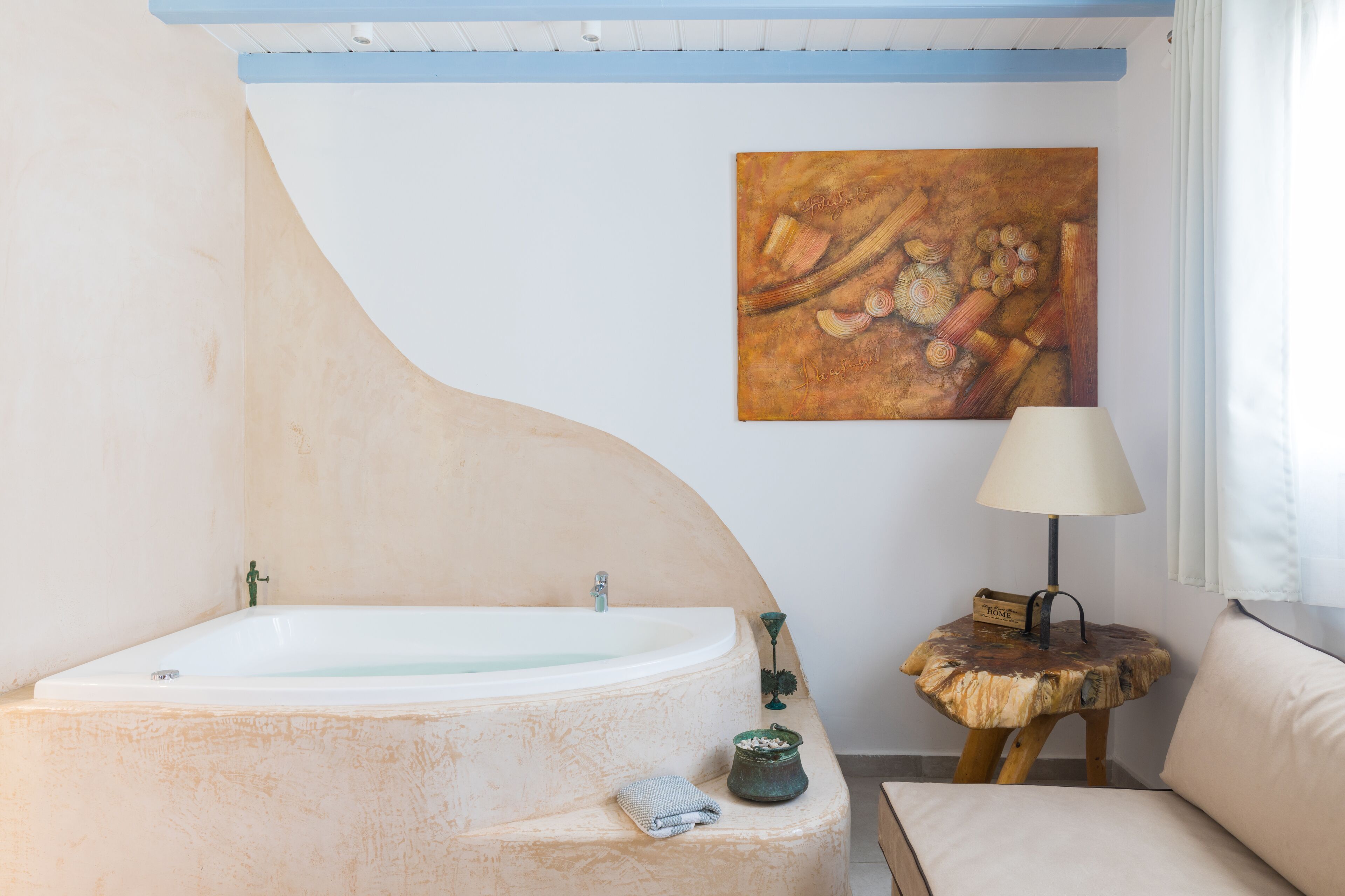 Une salle de bain avec une baignoire sur pieds, un tabouret en bois avec une lampe et un tableau au mur.