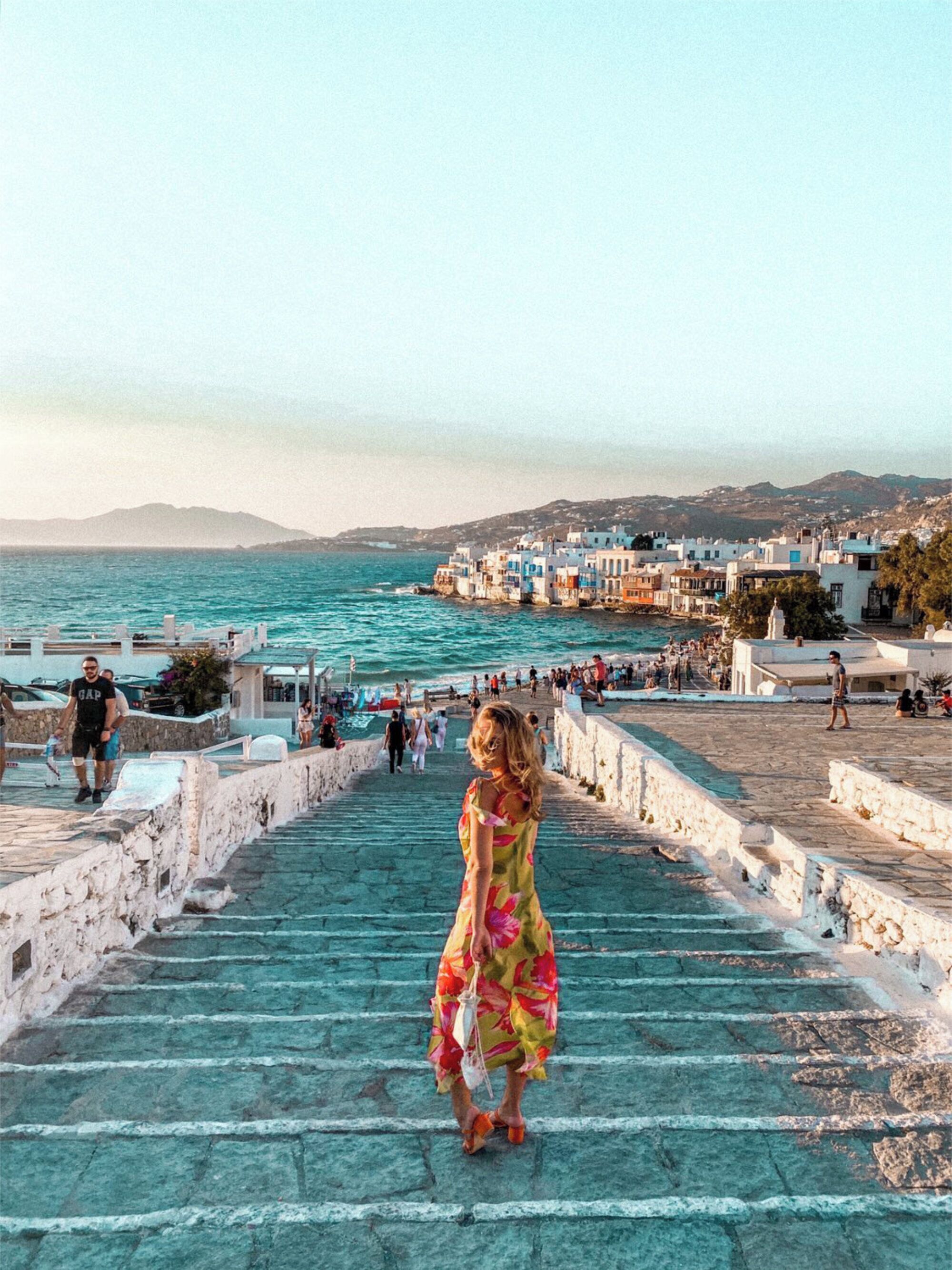 A woman descending a stone staircase with a view of a coastal town and the sea.