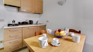 A kitchen with wooden cabinets, a dining table with white cups and saucers, and a fruit bowl. - Bed & Breakfast Giardini (Venice)