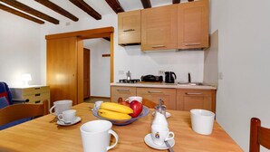 A dining area with a wooden table set for breakfast, including cups, saucers, and a fruit bowl. There is a coffee maker and a kettle on the table. The room has wooden cabinets and a wooden ceiling. - Bed & Breakfast Giardini (Venice)