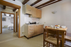 A kitchen with wooden cabinets, a dining table with chairs, and a view into a bedroom.