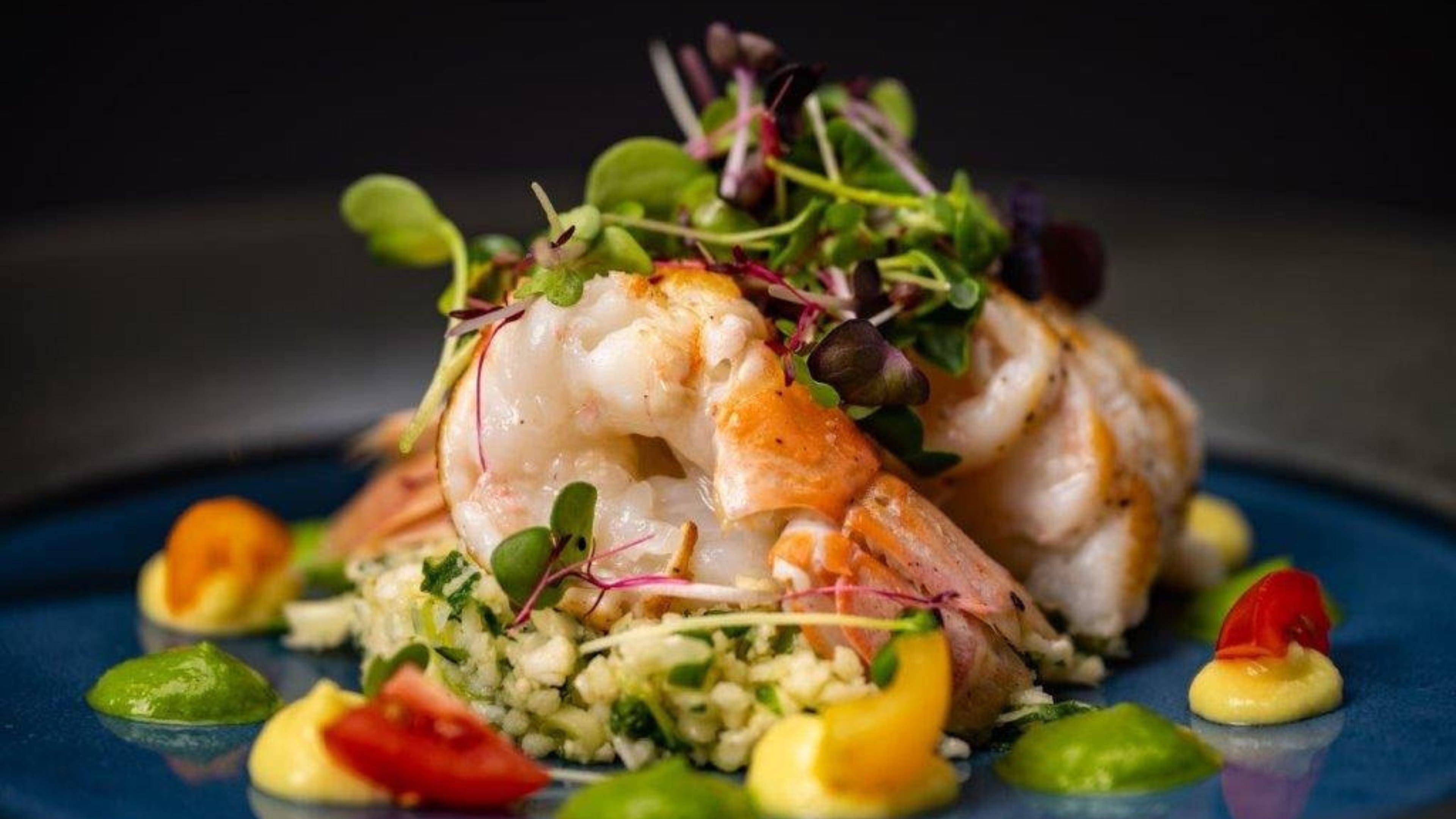 Un plato de comida con camarones, verduras y un plato azul.