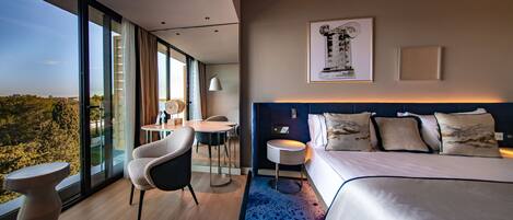 Una habitación de hotel moderna con una cama grande, un área de comedor y vistas al exterior.