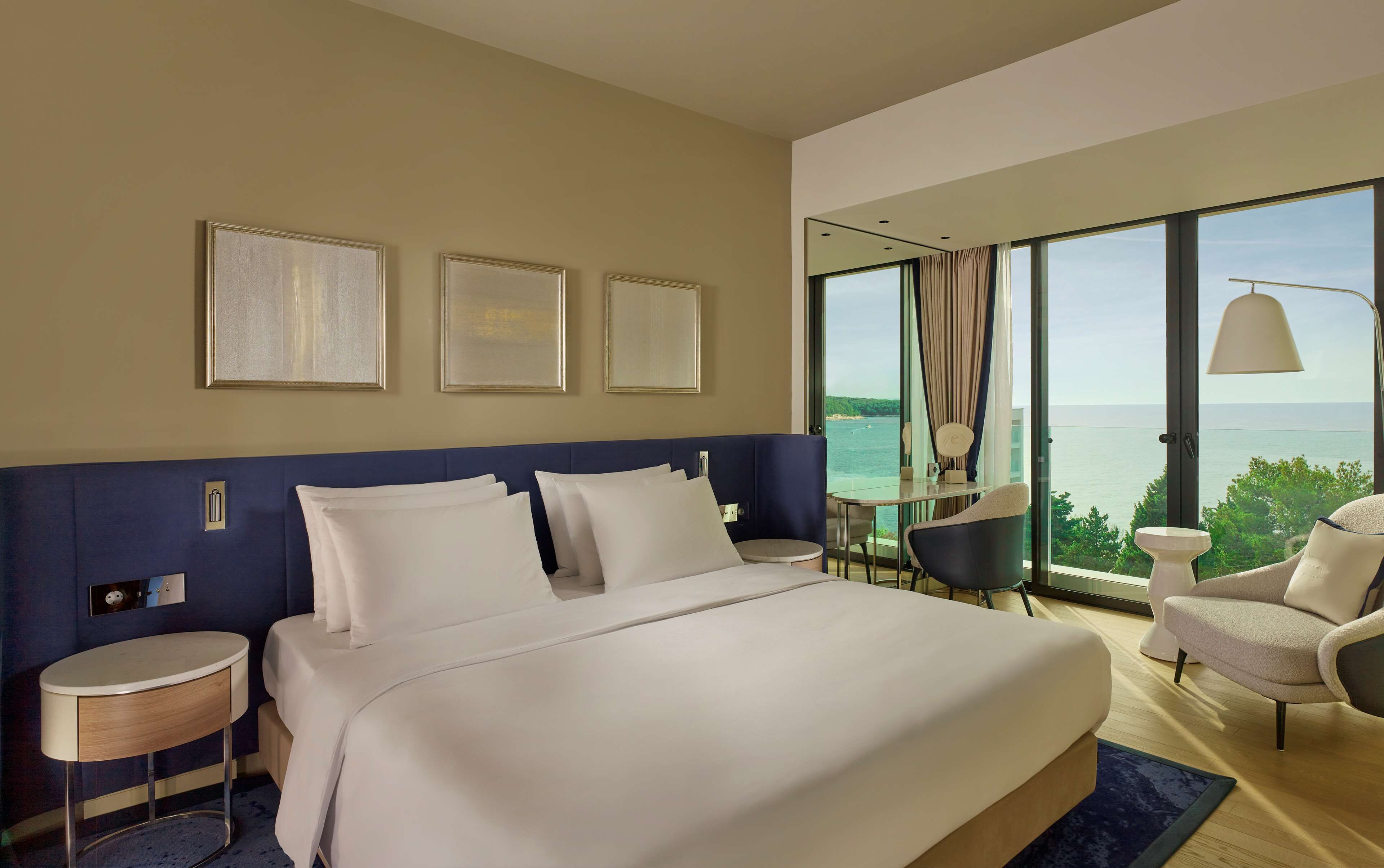 Habitación de hotel con una cama grande, un escritorio, una silla y vista al mar.