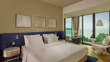 Habitación de hotel con una cama grande, un escritorio, una silla y vista al mar.