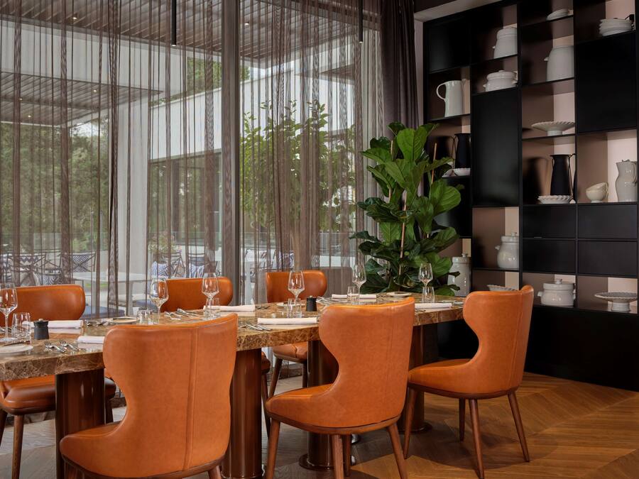 Un coin repas avec une table dressée pour quatre personnes, entourée de chaises orange, et une grande plante en pot en arrière-plan.
