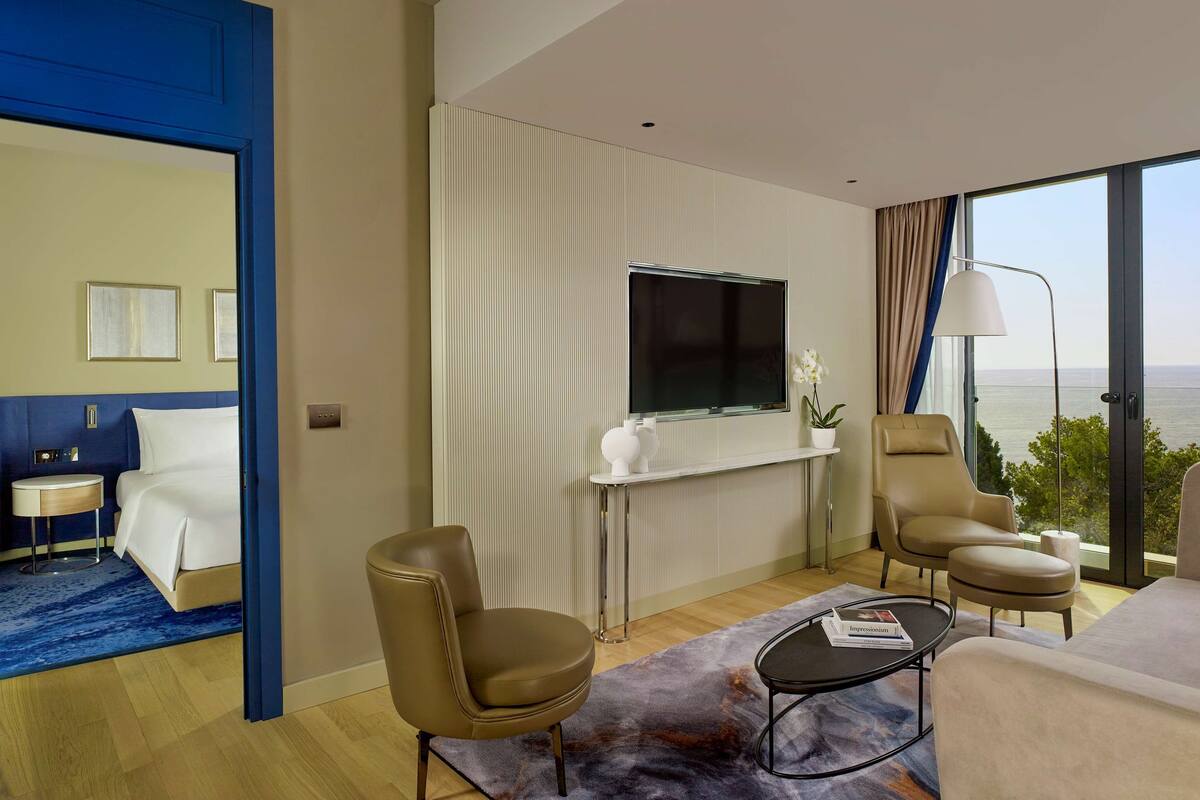 A hotel room with a bed, a TV, a sofa, a chair, and a view of the sea.