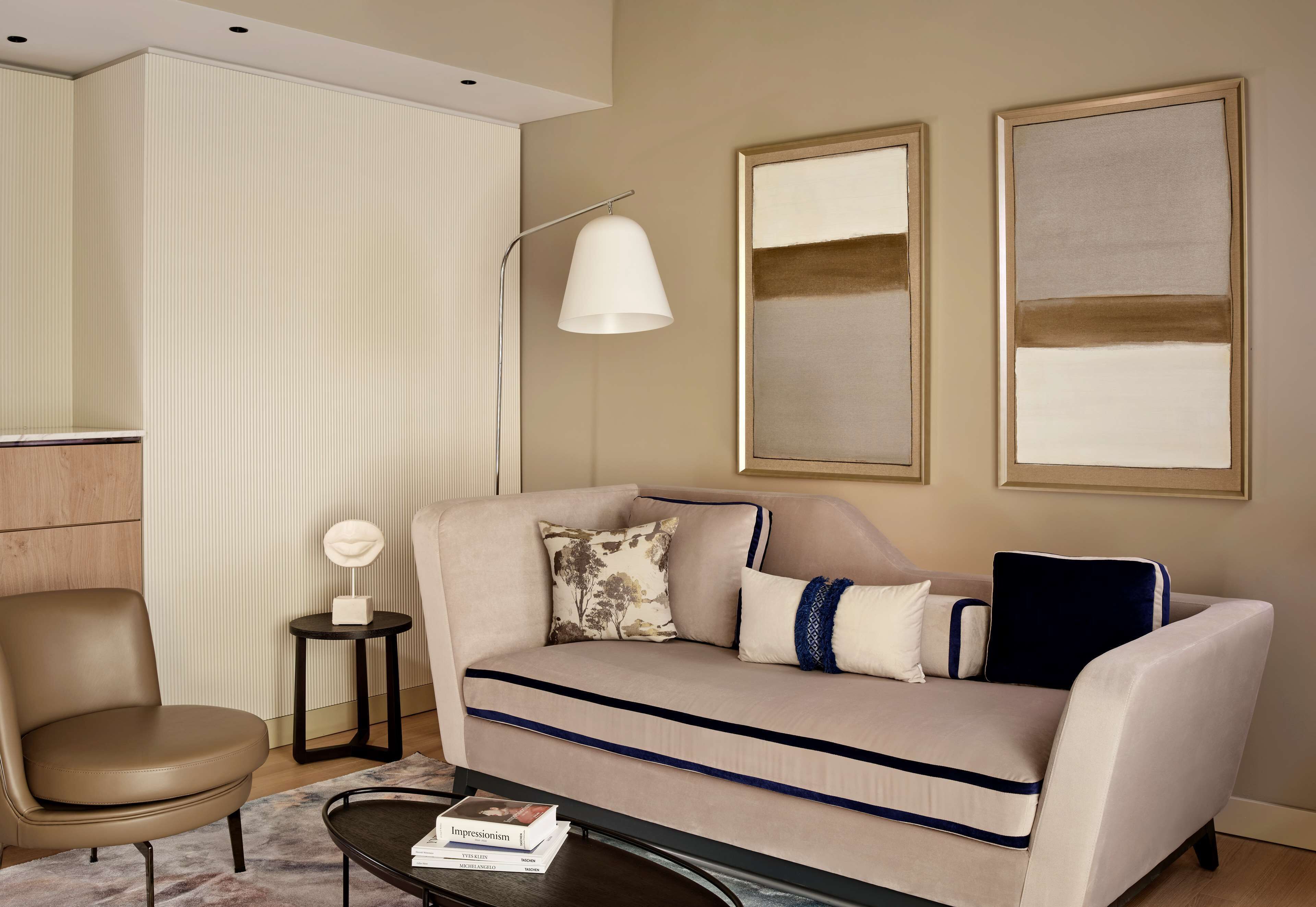A modern living room with a beige sofa, a side table, a floor lamp, and two abstract paintings on the wall.