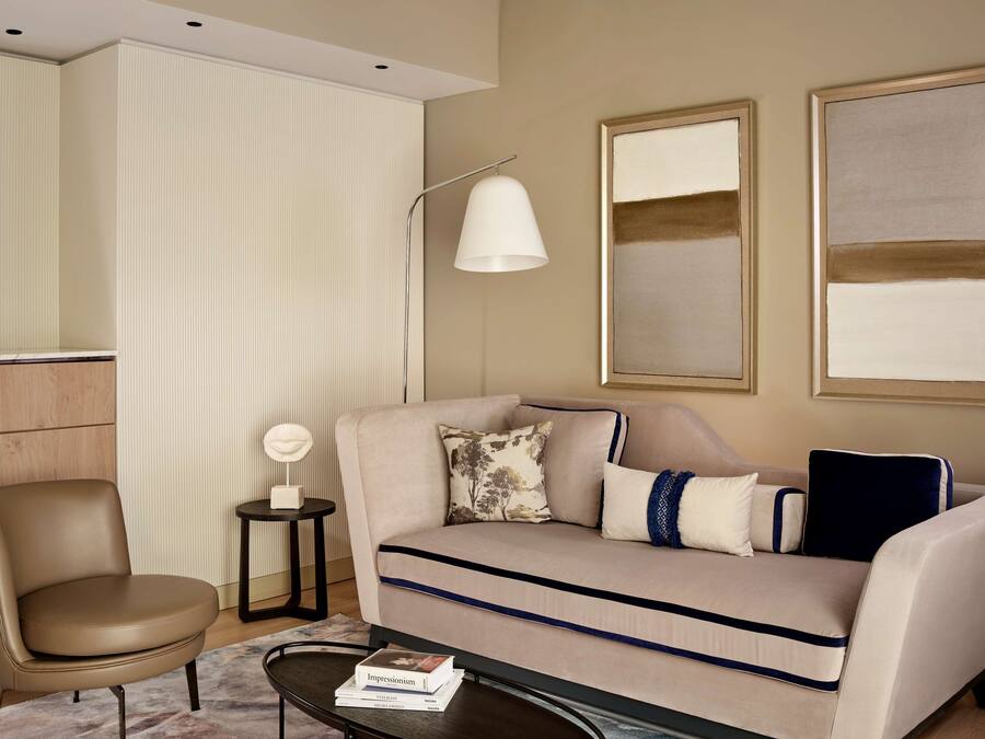 A modern living room with a beige sofa, a side table, a floor lamp, and two abstract paintings on the wall.