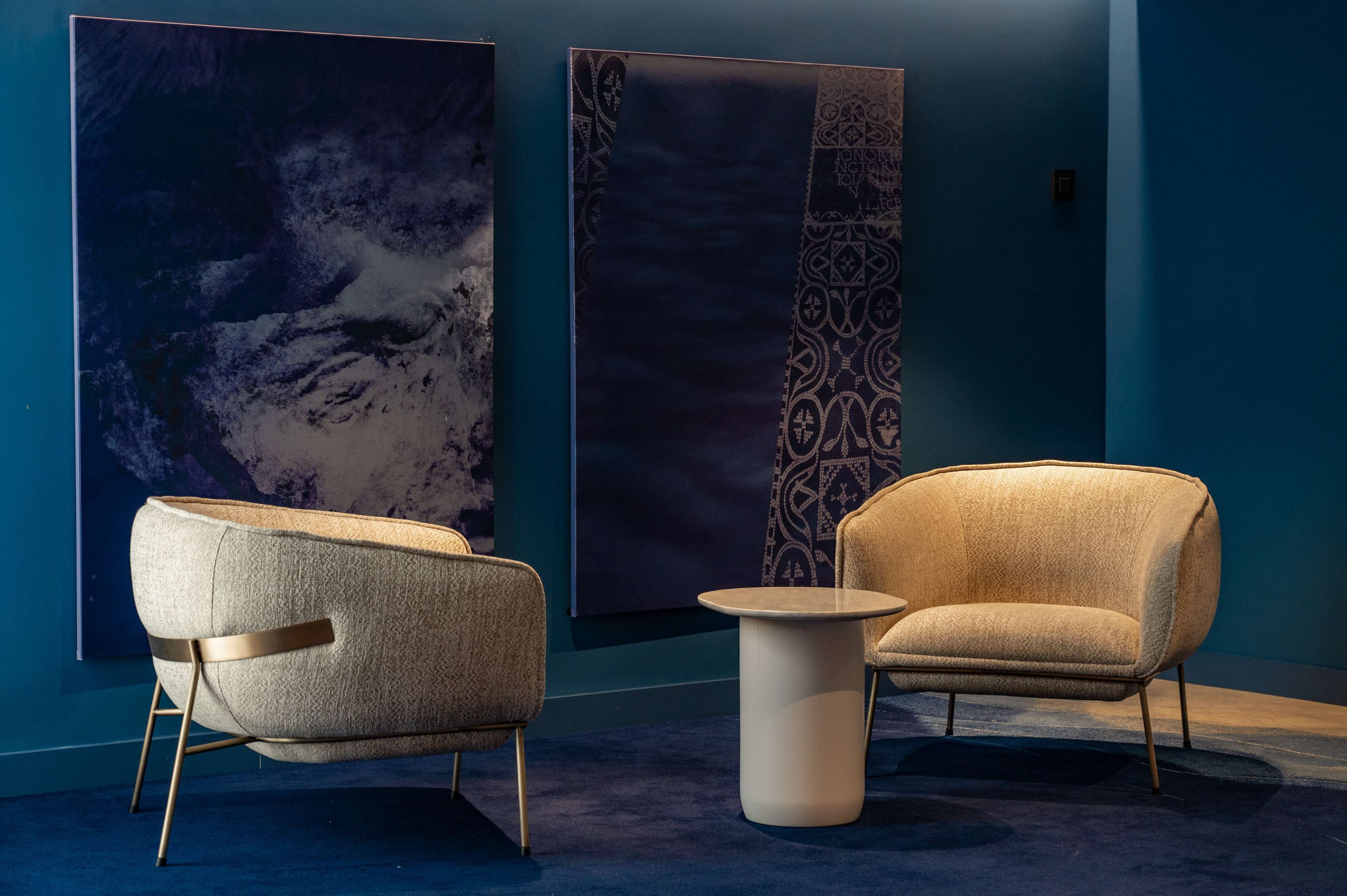 A modern room with two armchairs and a small table, a large abstract painting on the wall, and a patterned tapestry.