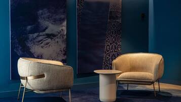 A modern room with two armchairs and a small table, a large abstract painting on the wall, and a patterned tapestry.