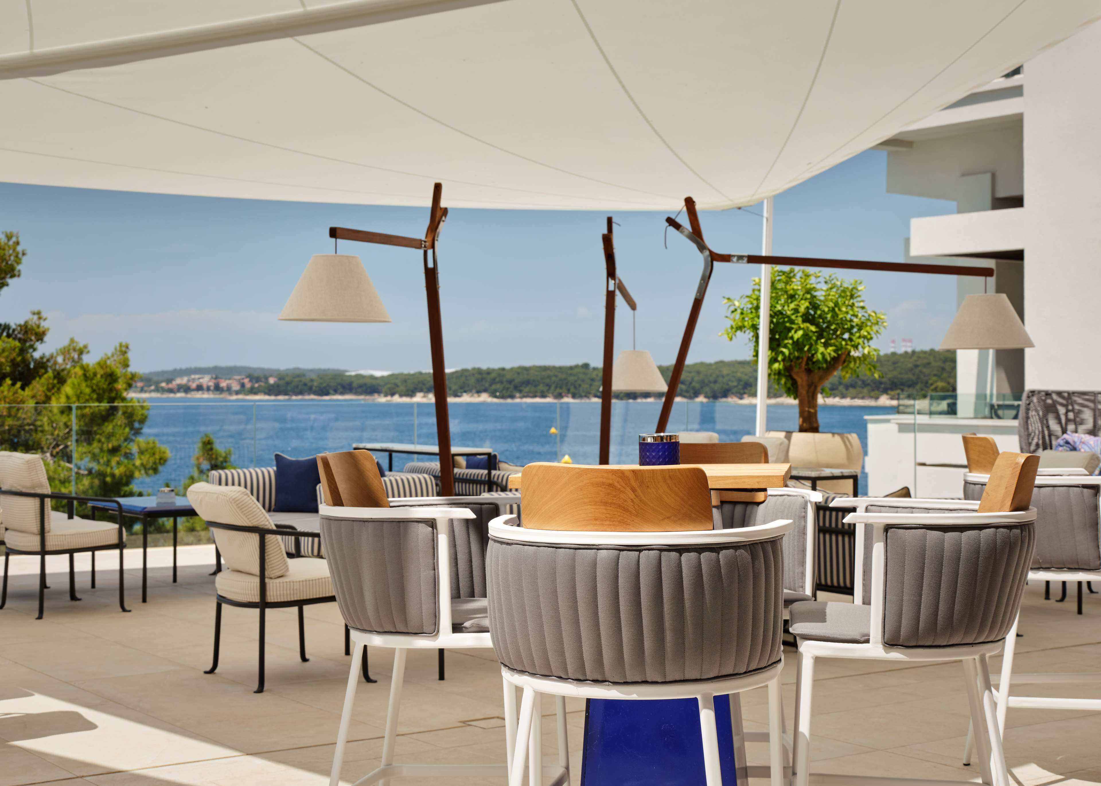 Une terrasse avec des sièges extérieurs, une vue sur la mer et un bâtiment moderne en arrière-plan.