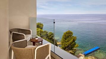 Un balcone con sedie in vimini, un tavolino e vista sul mare e sulla costa.