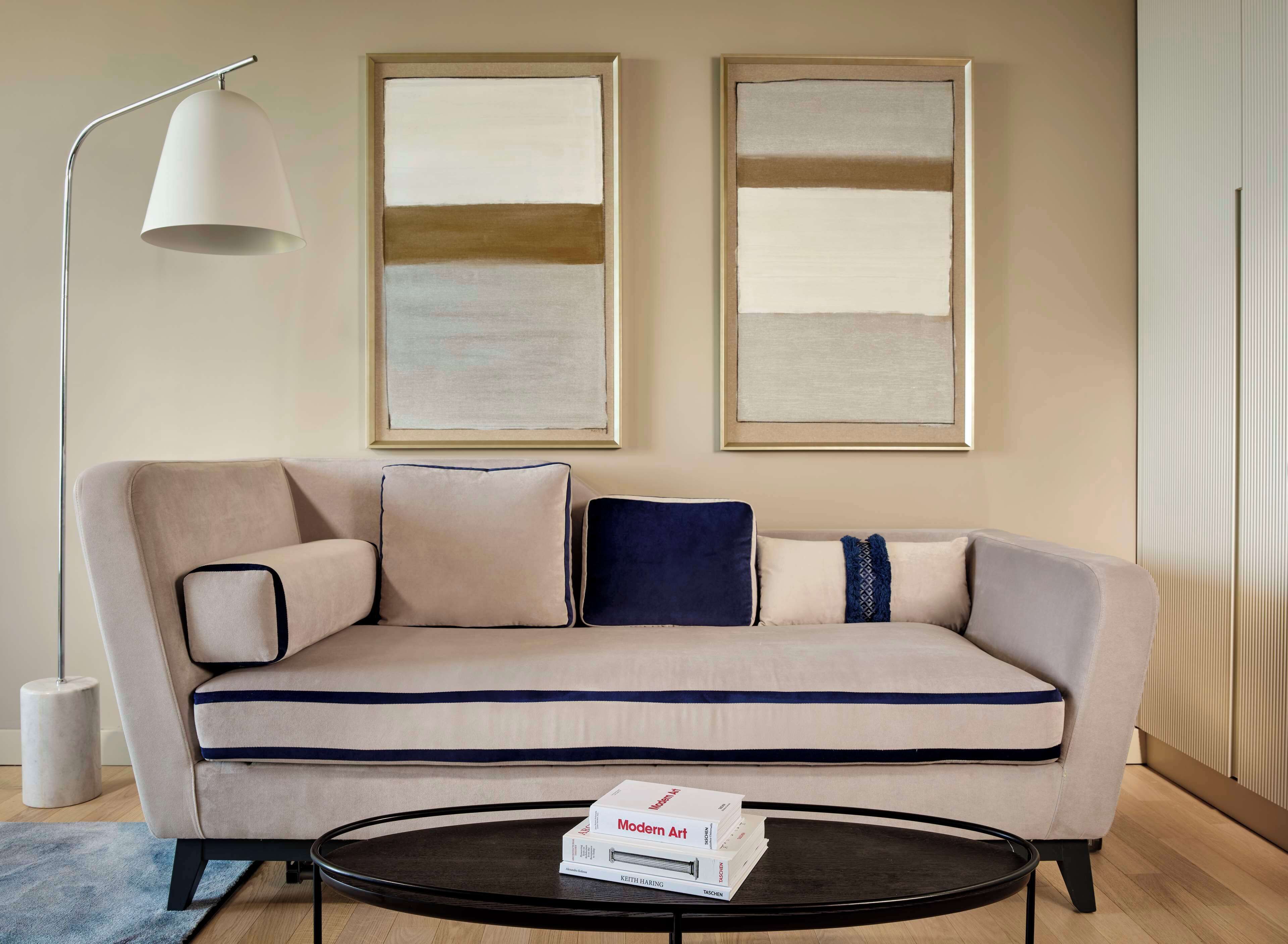 A modern living room with a beige sofa, a round coffee table, and two abstract paintings on the wall.