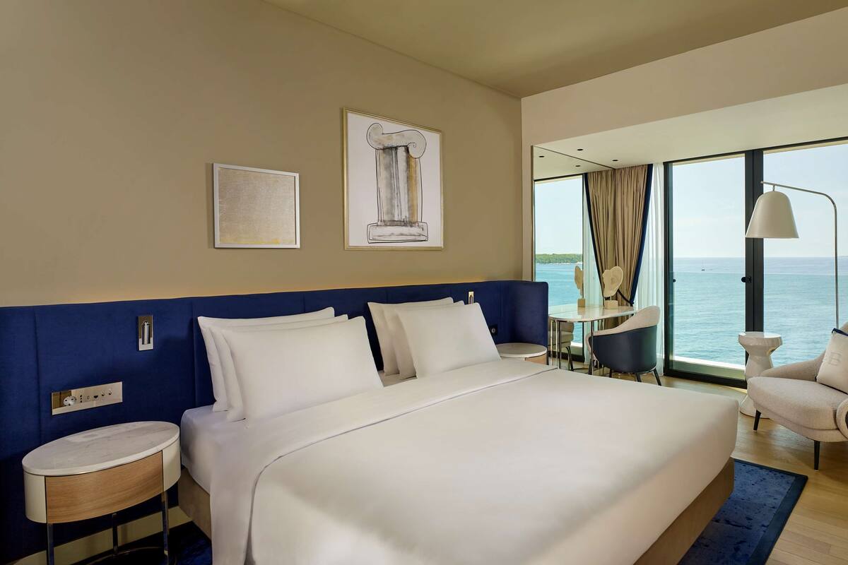 A hotel room with a large bed, a desk, a chair, and a view of the sea.