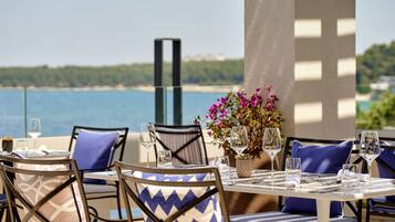 Un'area pranzo all'aperto con tavoli e sedie, vista sul mare e un'elegante composizione floreale.