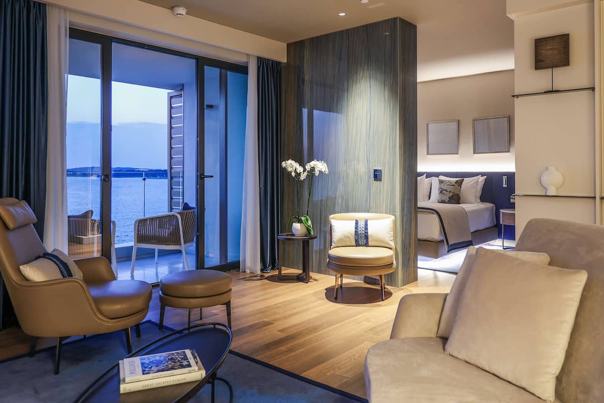 A modern hotel room with a balcony, leather sofas, a small table, and a view of the sea.