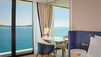 A modern hotel room with a large window overlooking the sea, a bed, a small round table, and a chair.