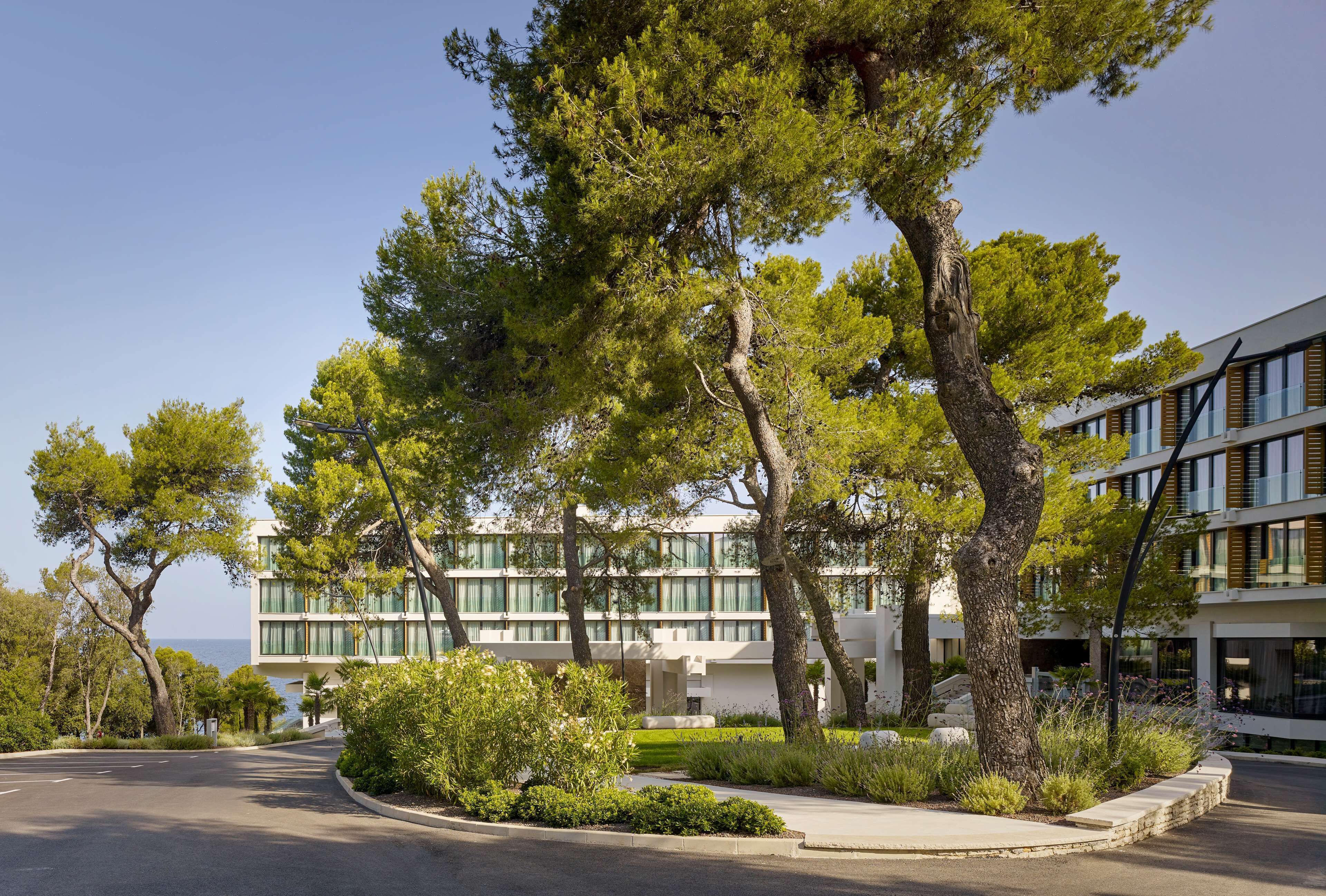 A modern building with large windows and a landscaped garden with trees and shrubs.