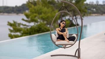 A person sitting in a hanging chair by a pool with a view of the water and trees.
