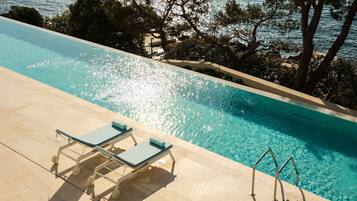 A swimming pool with clear blue water, surrounded by trees and a view of the sea.