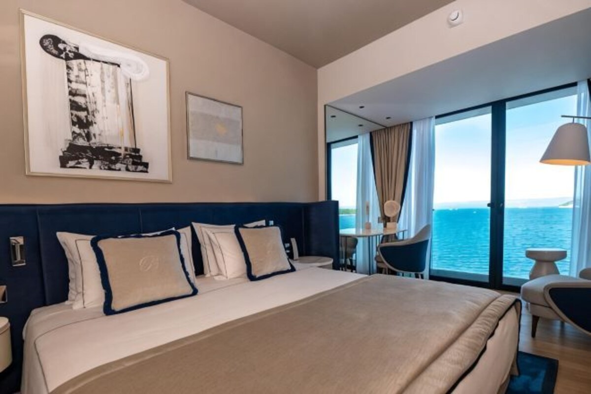 Une chambre d’hôtel avec un grand lit, une vue sur la mer, un coin repas et un balcon.