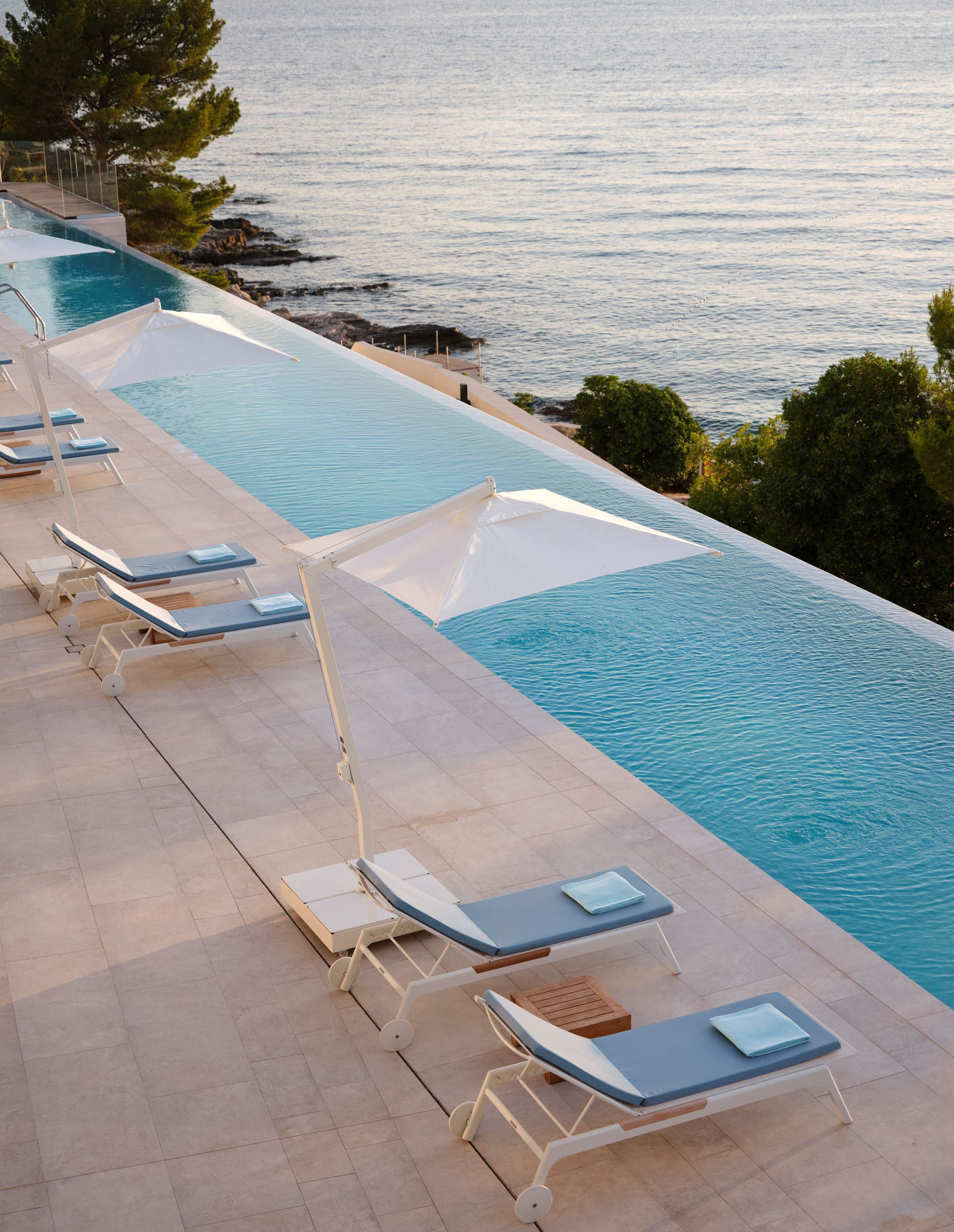 A poolside area with sun loungers and umbrellas, overlooking a body of water.