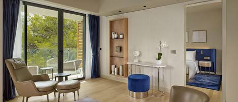 Une chambre d’hôtel moderne dotée d’un balcon, d’un coin salon avec un canapé et des fauteuils, d’une petite table et d’un lit avec une tête de lit.