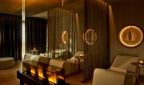 A modern hotel room with a fireplace, a sofa, a bed, and a round mirror with a candle on a side table.