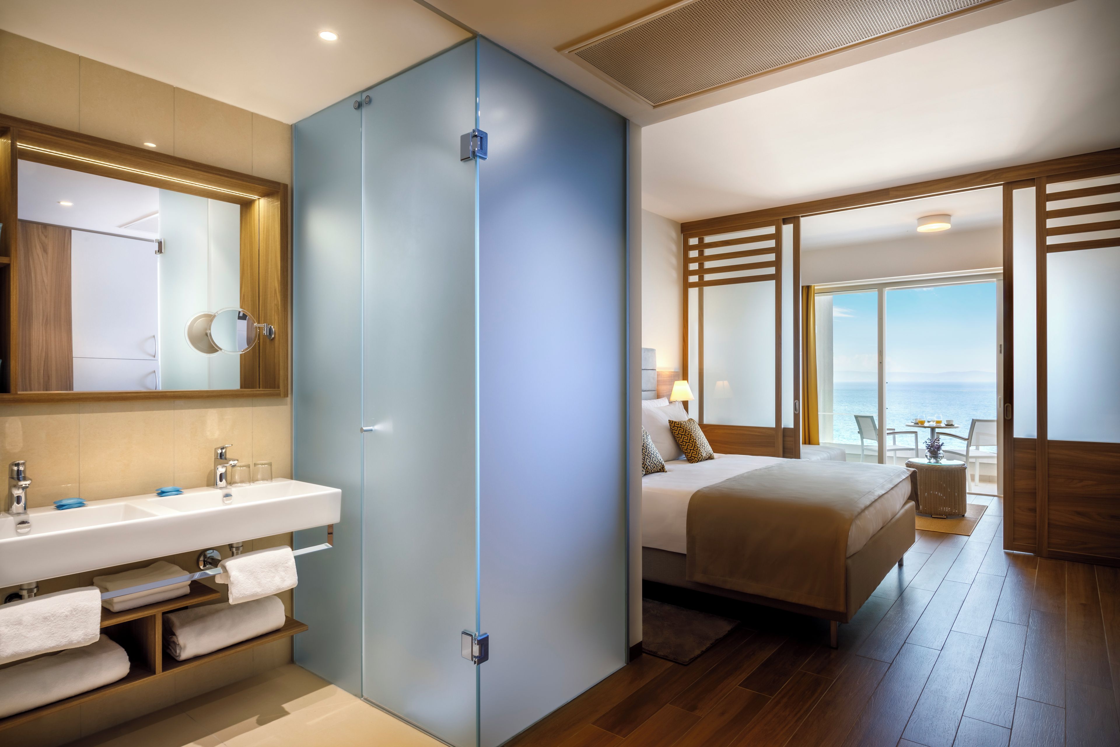 A modern hotel room with a bathroom, a bed, and a view of the sea.