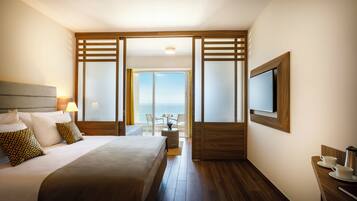 A hotel room with a bed, a TV, a desk with a coffee maker, and a view of the sea.
